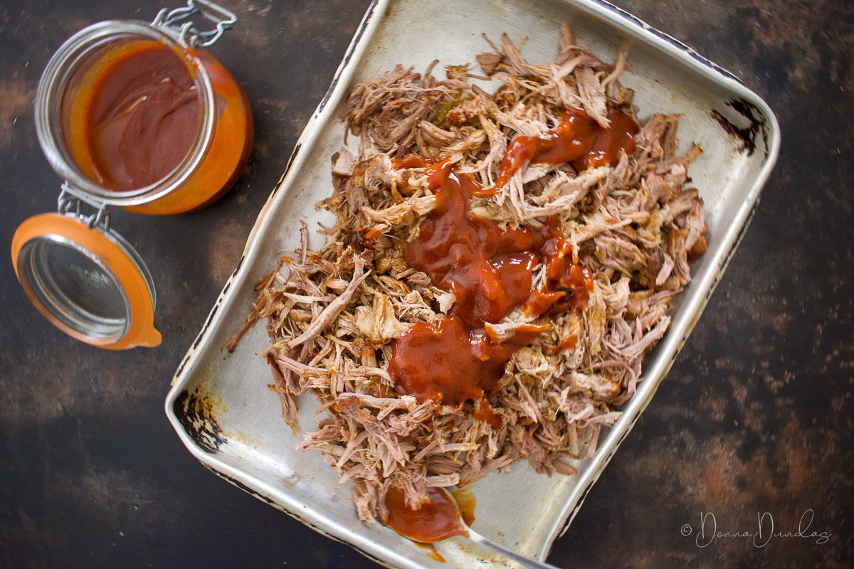 silver tray of shredded pork with bbq sauce drizzled on top.