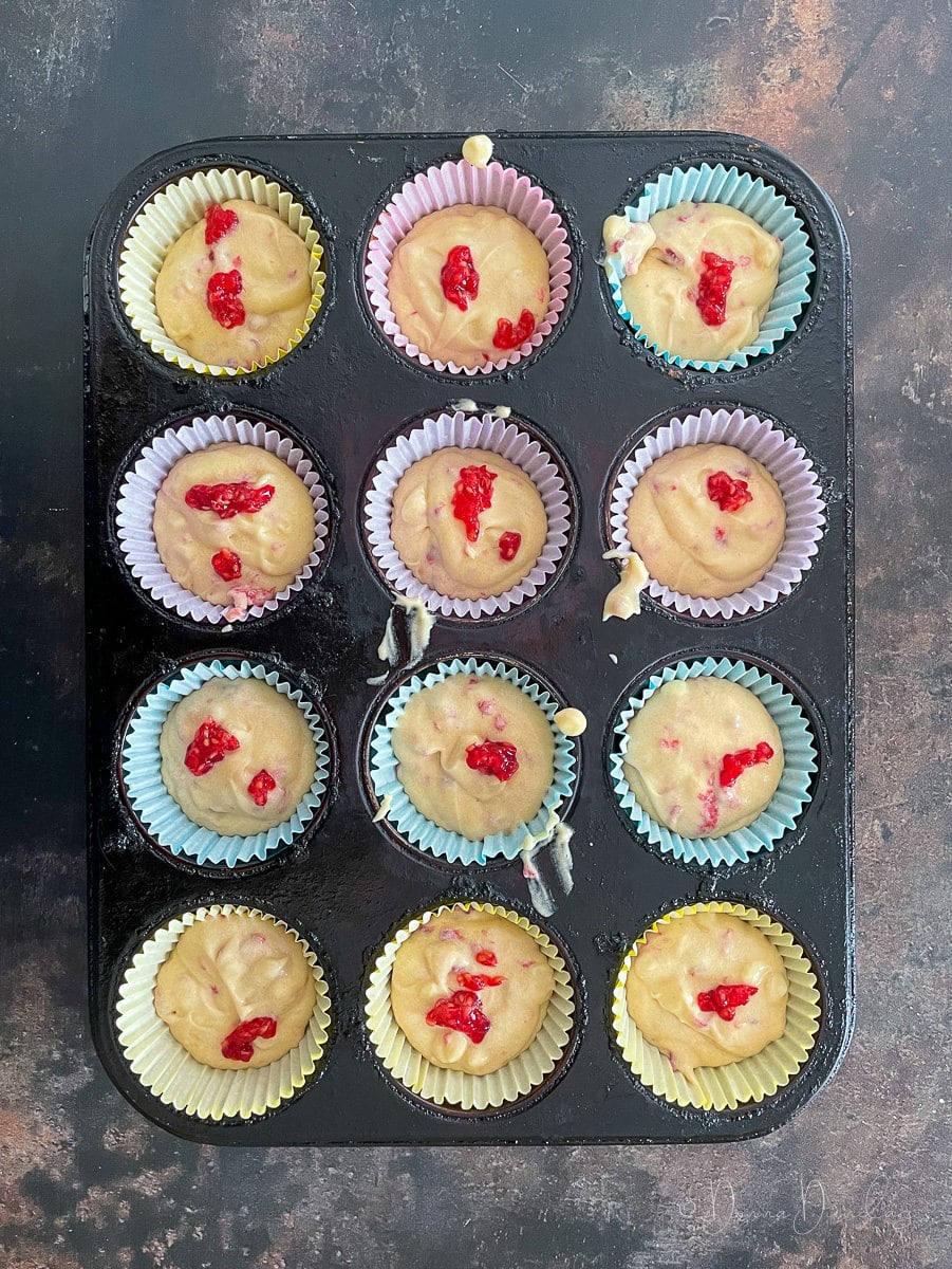 unbaked raspberry and white chocolate cupcakes in paper cases in muffin tin.