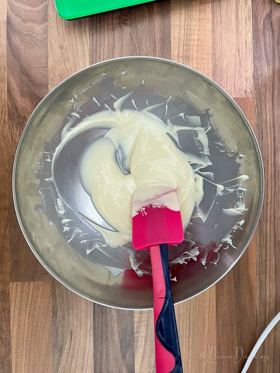 melted white chocolate in silver mixing bowl with pink spatula.