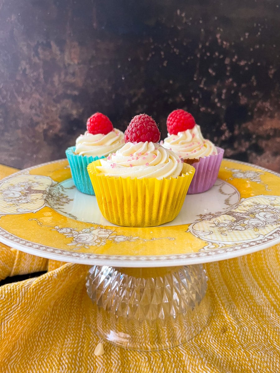 3 cake topped with raspberries in colour paper cases on vintage yellow cake stand.