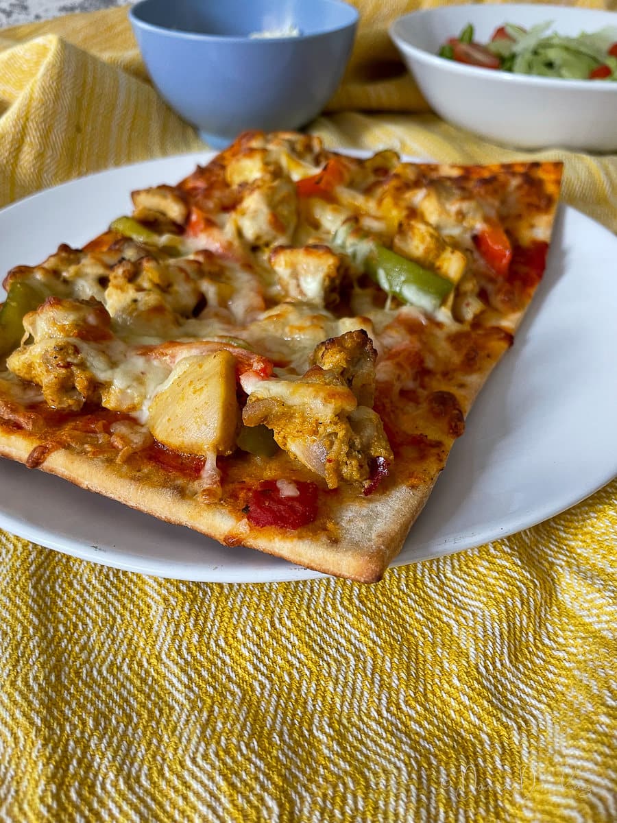 Side view of chicken tikka pizza with peppers on white plate.