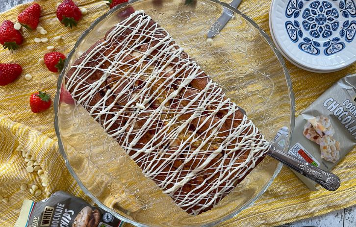 top view of strawberry and white chocolate loaf cake drizzled with white chocolate on glass cake stand.