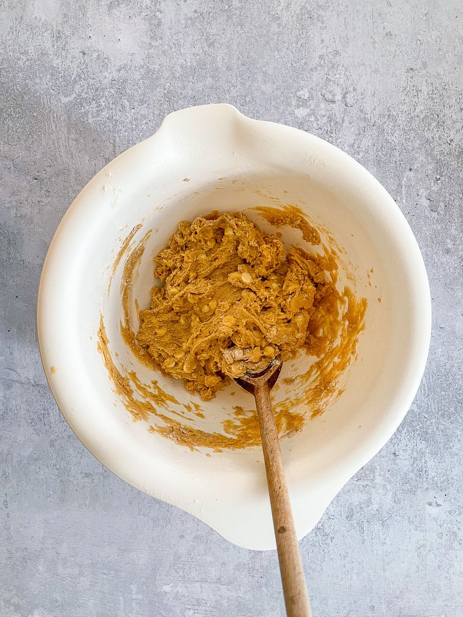 white chocolate chip cookie dough in white mixing bowl with wooden spoon.