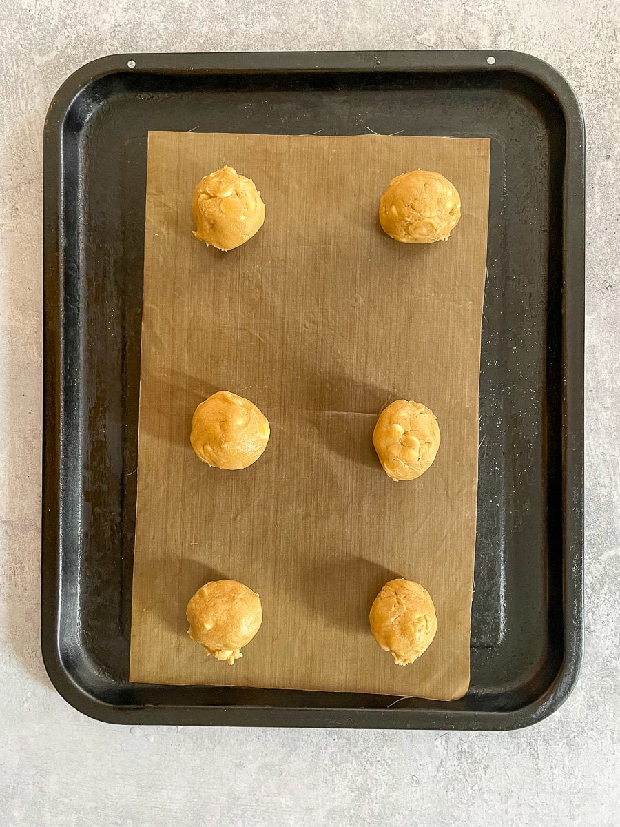 balls of white chocolate chip cookie dough on baking tray with reusable baking paper.