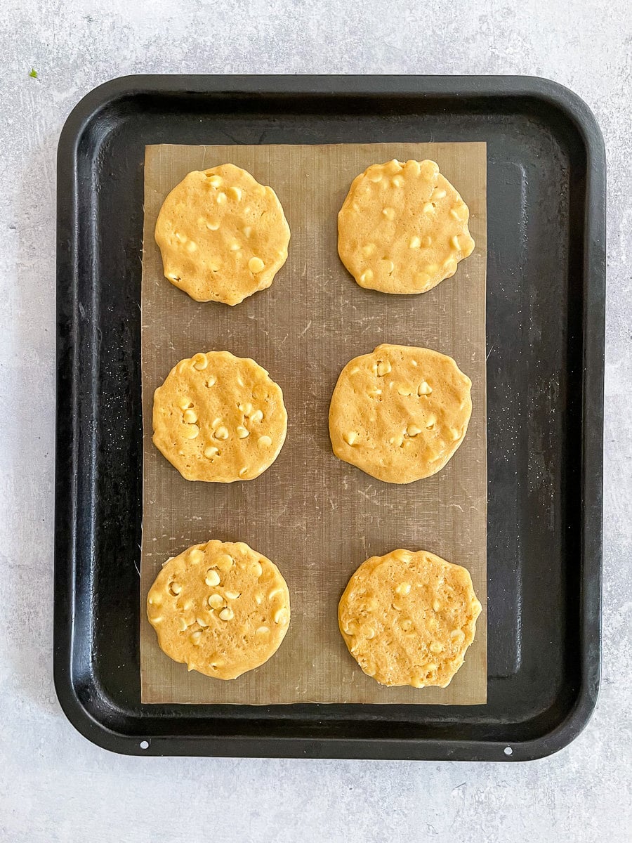 unbaked cookies with white chocolate chips on baking tray.