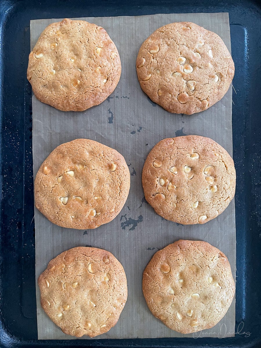 6 baked white chocolate chip cookies on baking tray.