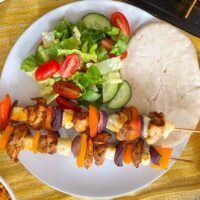 2 chicken and halloumi skewers served on a plate with salad and pitta bread.