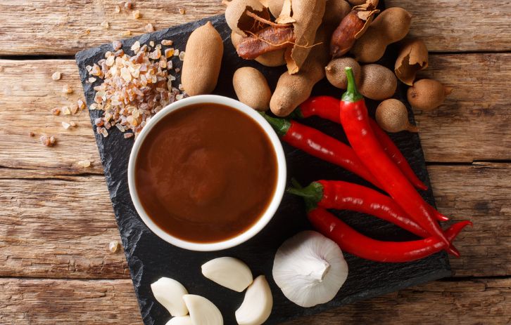 Delicious spicy tamarind sauce closeup in a bowl on a wooden table. horizontal top view from above.