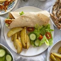 Chicken and halloumi wrap on plate with potato wedges and salad.