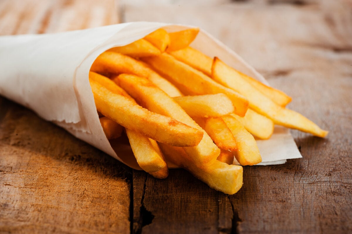 Potatoes fries in a little white paper bag on wood board.