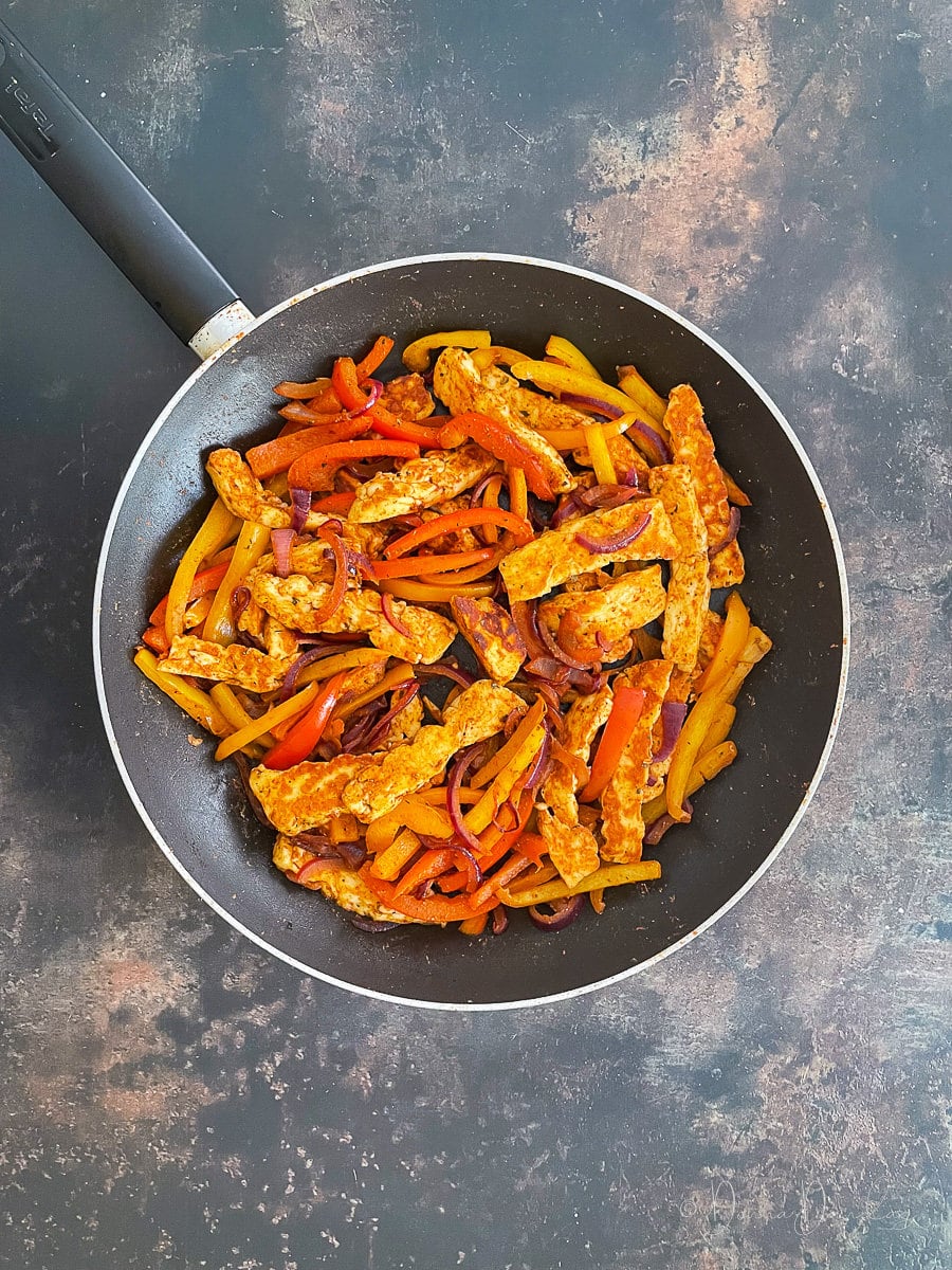 sliced onion, pepper and halloumi tossed in fajita seasoning in frying pan.