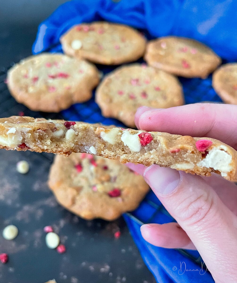close up of middle of broken cookie. White chocolate chips and raspberry pieces visible.