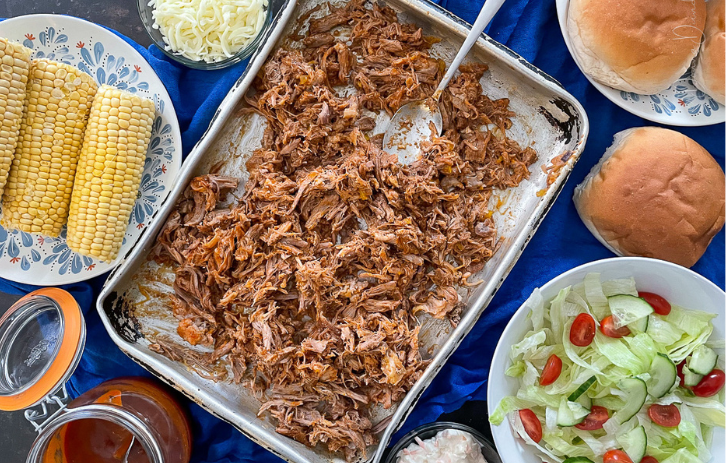 Pulled pork on a metal tray. Corn, salad, cheese and bread to the sides.