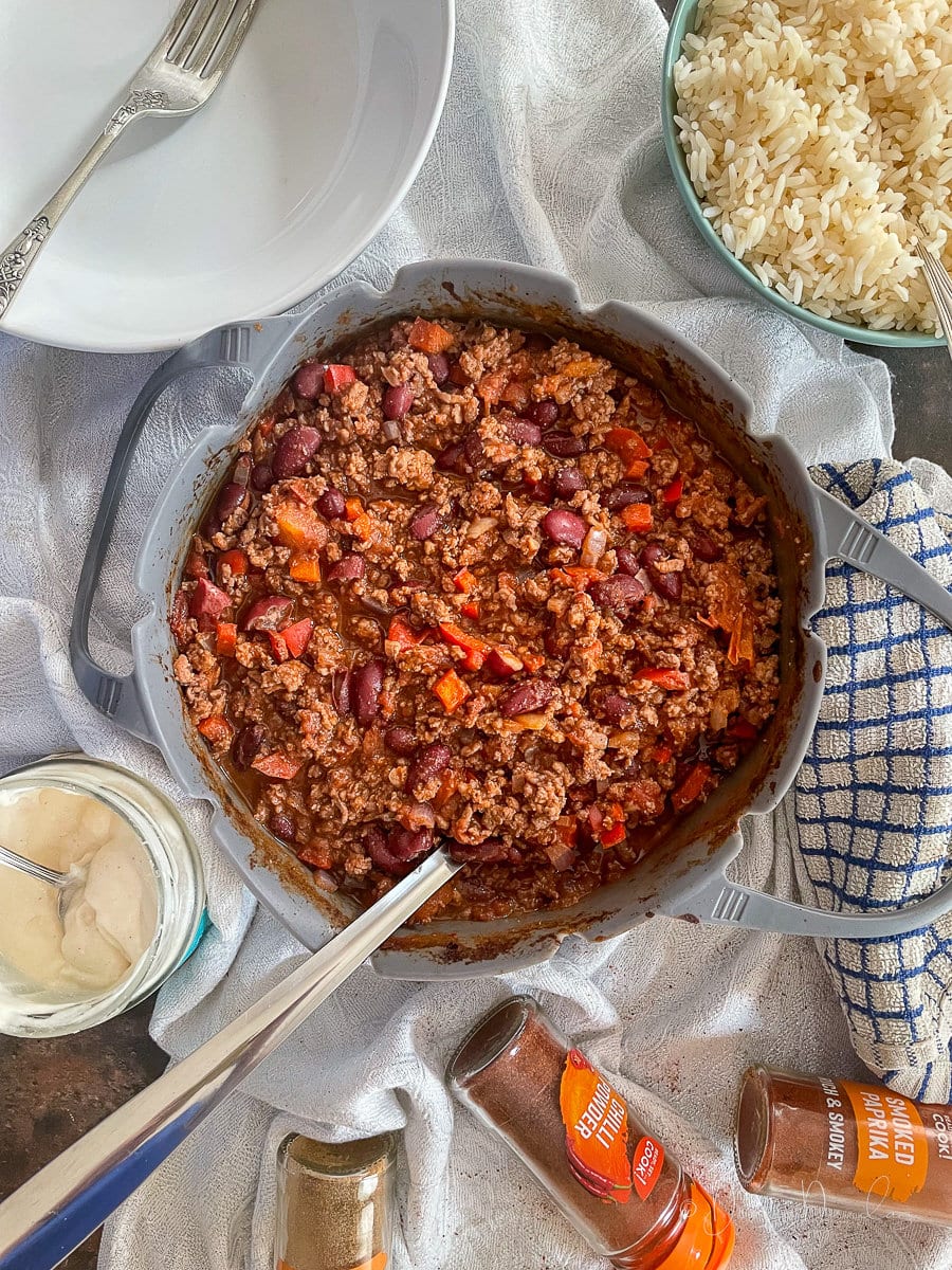 Air Fryer Chilli in silicone dish with serving spoon. Served potion to the side. Rice, soured cream and spices also on table.