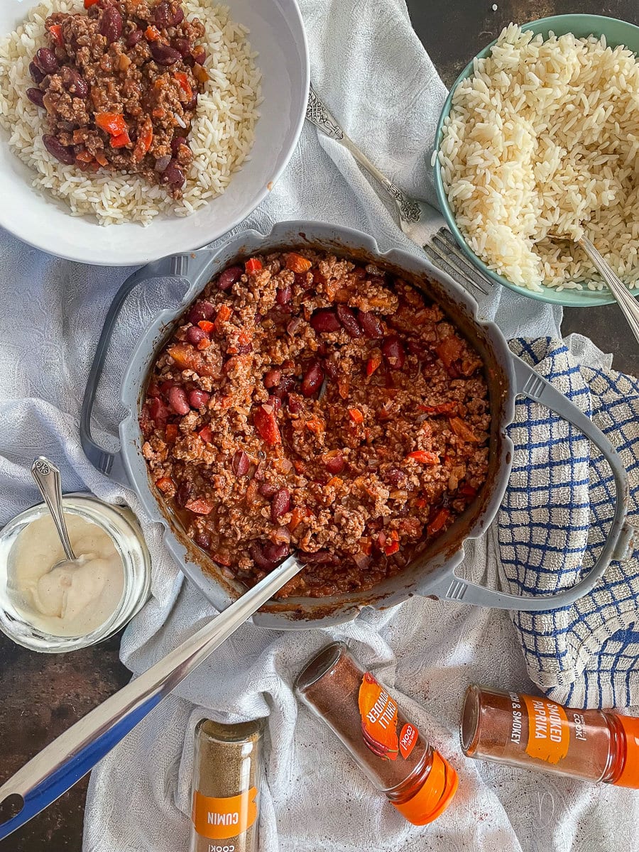 Air Fryer Chilli in silicone dish with serving spoon. Served potion to the side. Rice, soured cream and spices also on table.