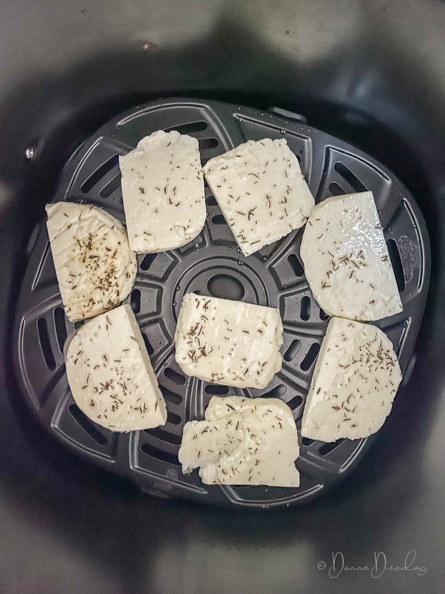 uncooked halloumi slices in air fryer basket.