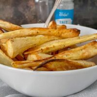 Roasted air fryer parsnips in white bowl with fork.