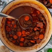 Beef and chorizo Stew in cast iron dish with serving spoon.