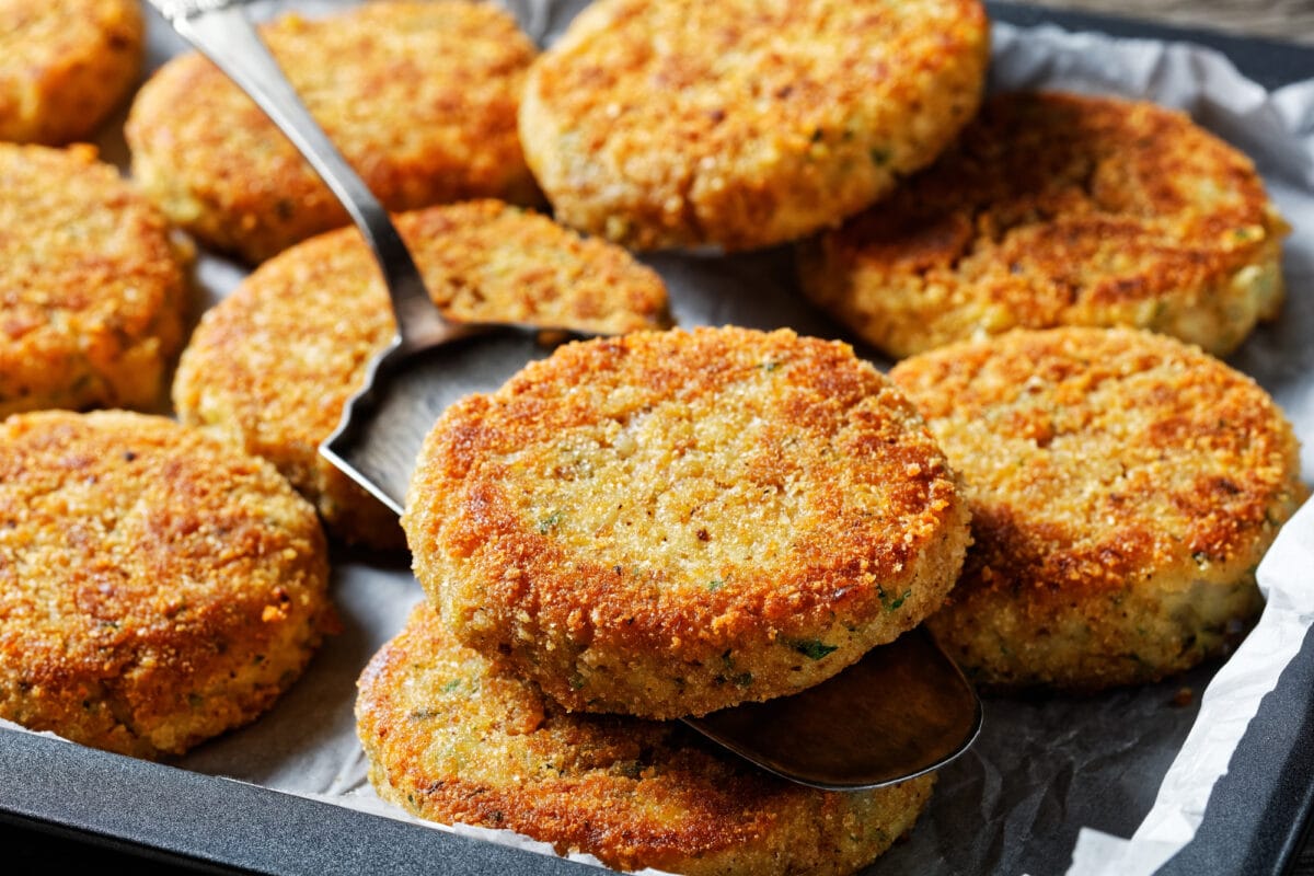 White fish cakes of white fish fillet: cod or haddock with potato and parsley, breaded in breadcrumbs and then baked in the oven, served on a sheet pan on a wooden background, top view, close-up.