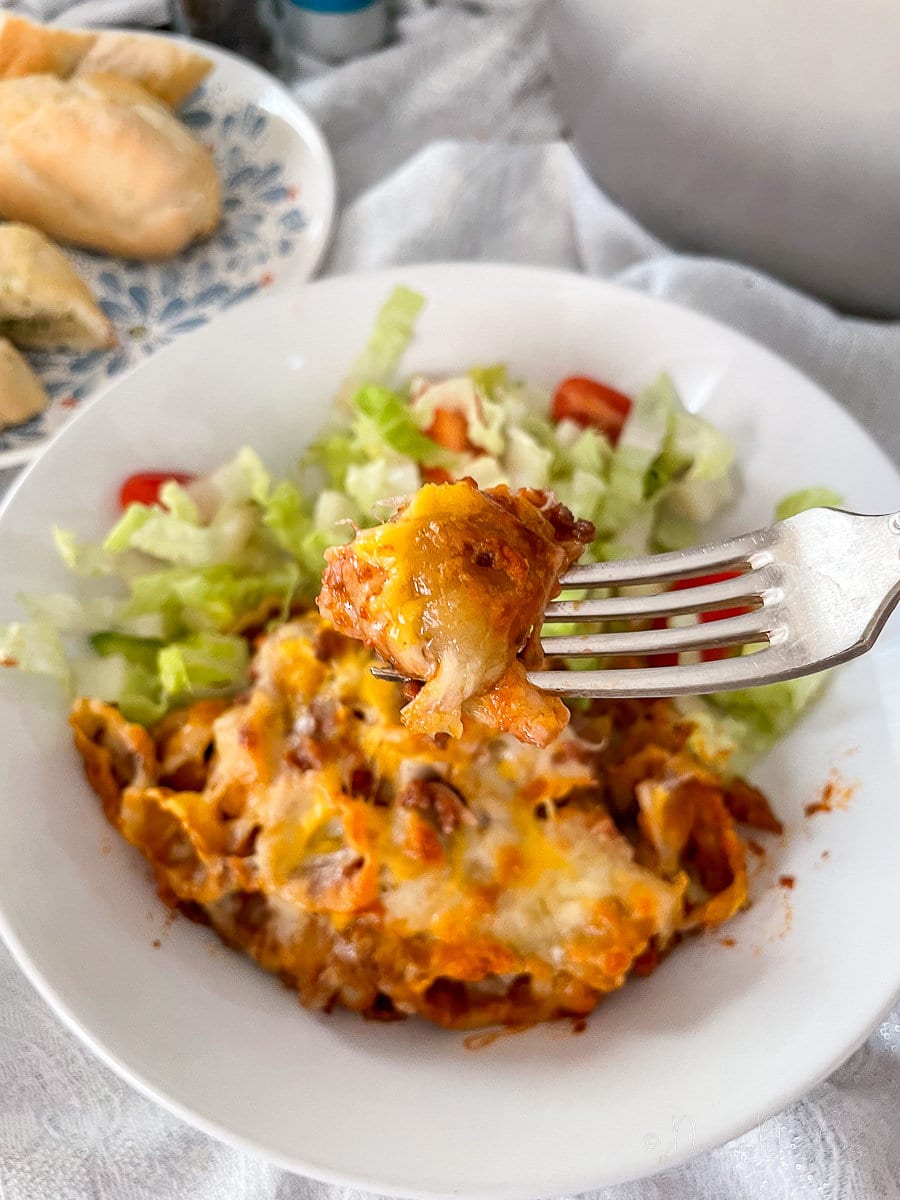 close of of piece of cheese pasta on fork. Pasta bake and salad in bowl behind.