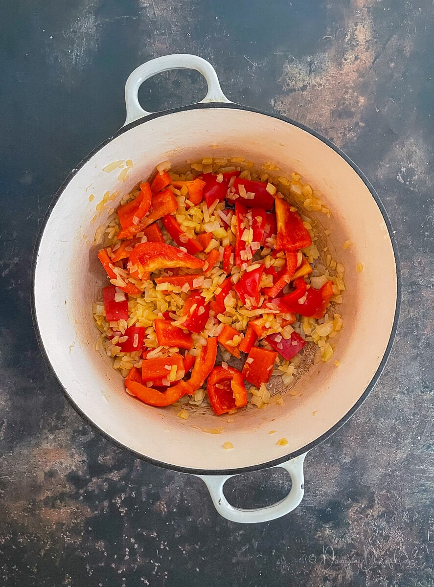 diced onions and sliced peppers in cast iron dish.