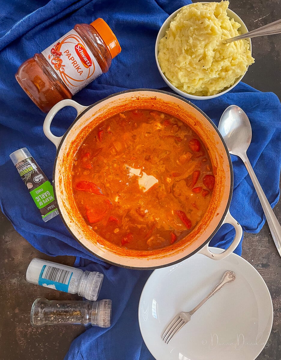 Chicken Goulash with Soured Cream in a large cast iron cooking dish. Mash potato and ingredients to the sides.