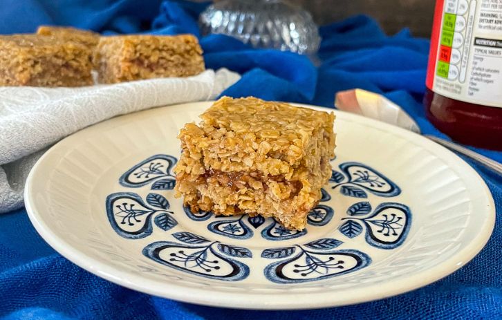square of flapjack with jam in the middle on small blue patterened plate.