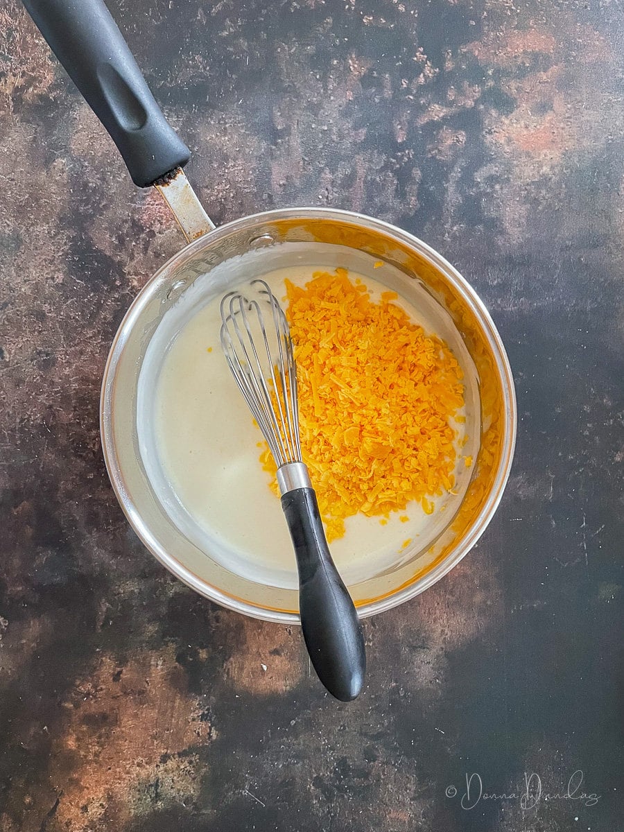 white sauce with grated cheese in pan with whisk.