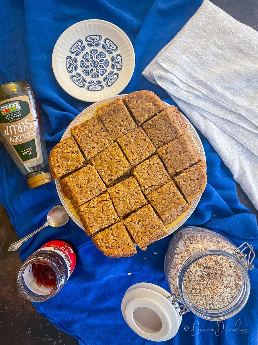 air fryer flapjack cut into squares on cake stand. Ingredients to the sides.
