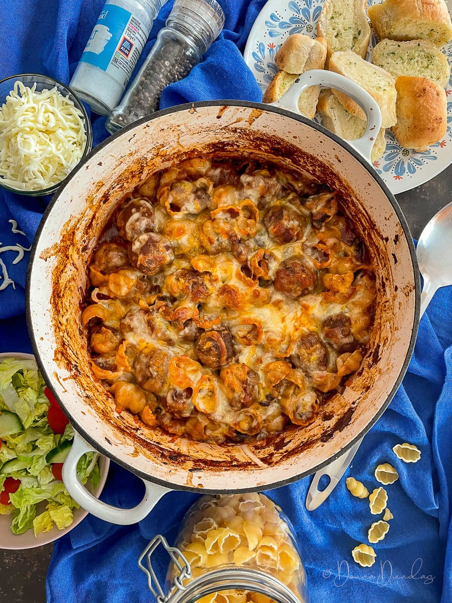 meatball pasta bake on table with salad and garlic bread.