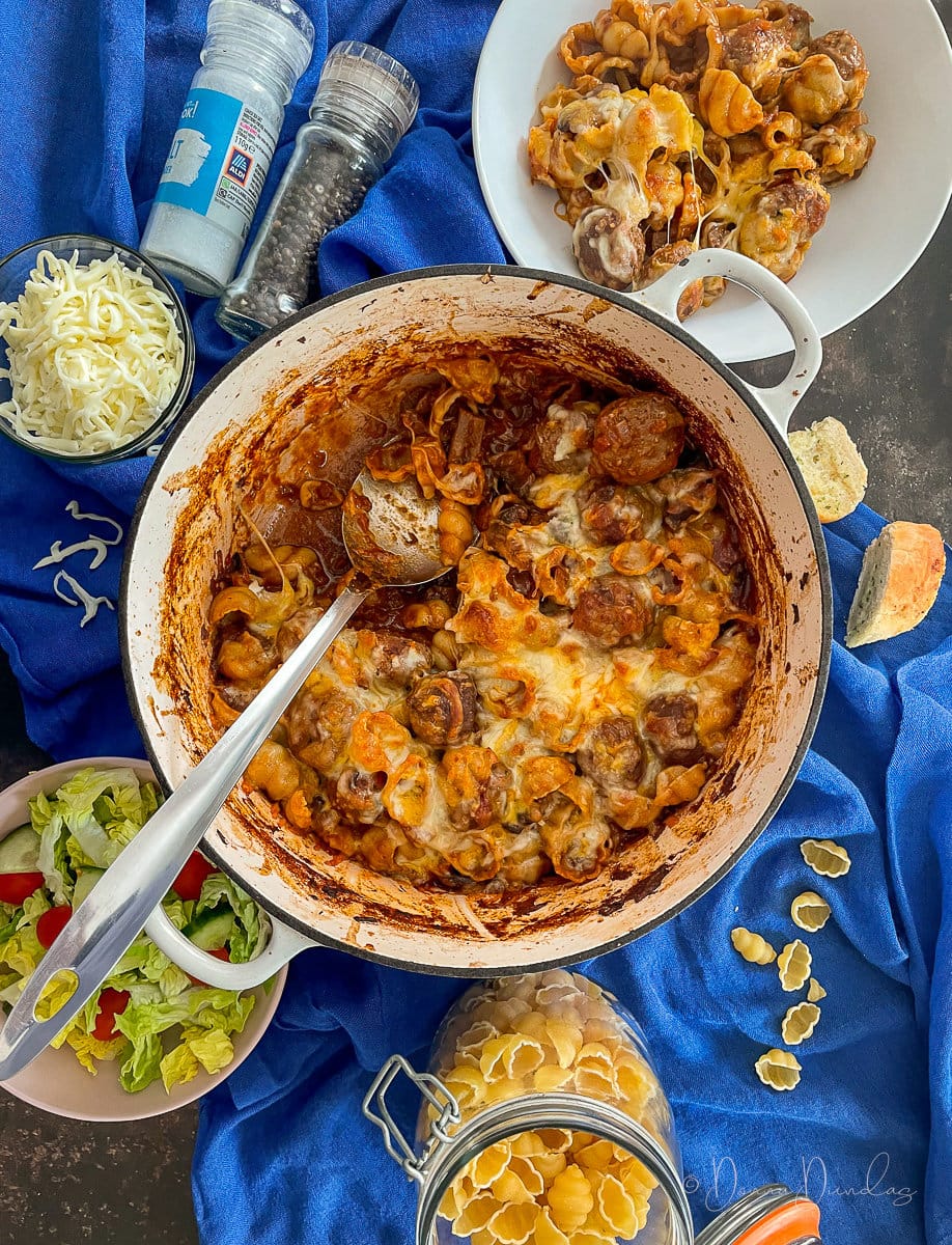 meatball pasta bake on table with salad and garlic bread. Served portion to the side.