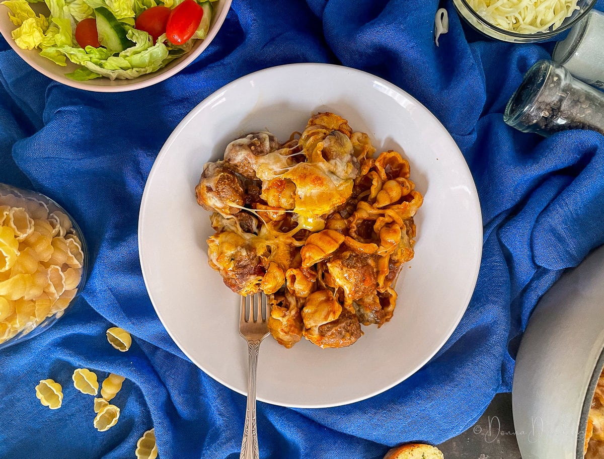 close up of meatball pasta portion in white bowl with fork.