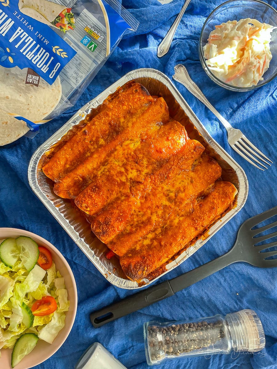 air fryer enchiladas in foil tray on table with sides.