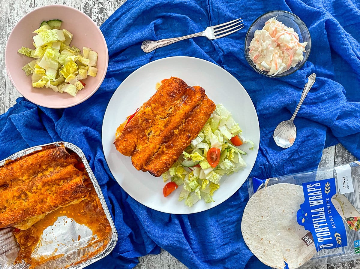 enchiladas on plate with salad. Cooking tray and sides also on table.