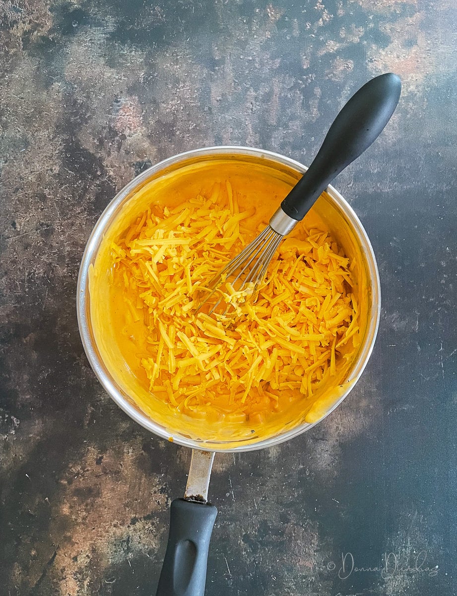 grated cheese in cheese sauce in saucepan with whisk.