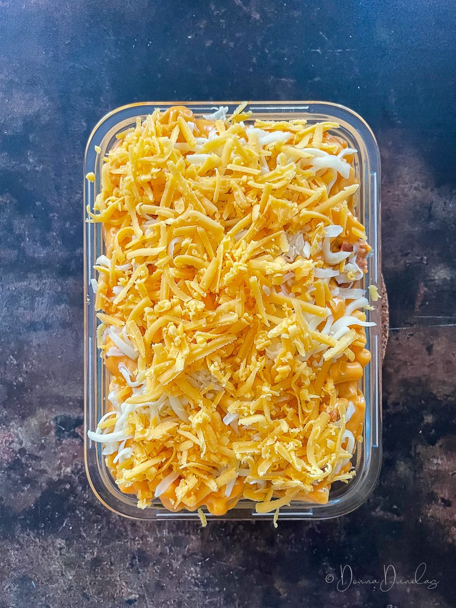 unbaked Mac and cheese in glass cooking dish with grated cheese.
