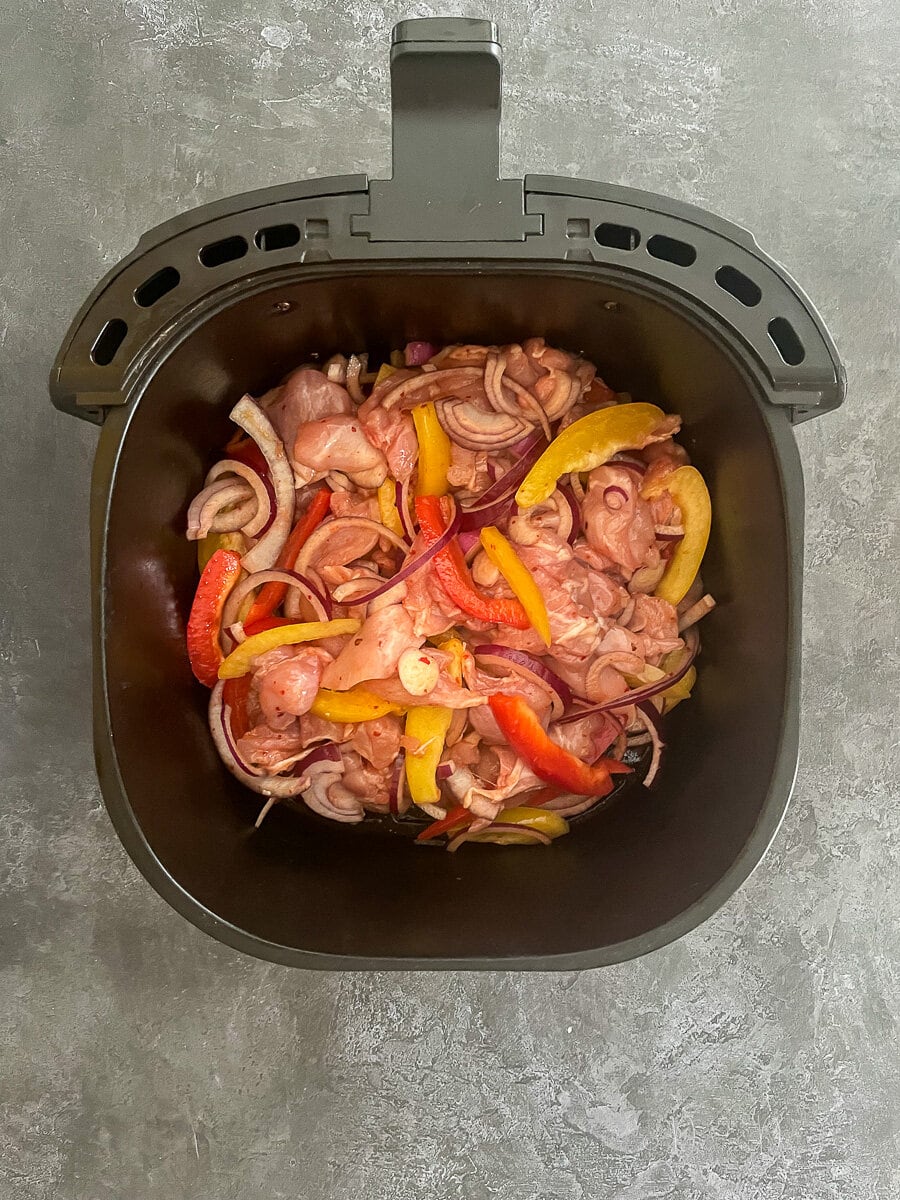 uncooked chicken, peppers, onion and honey chilli sauce in air fryer basket.