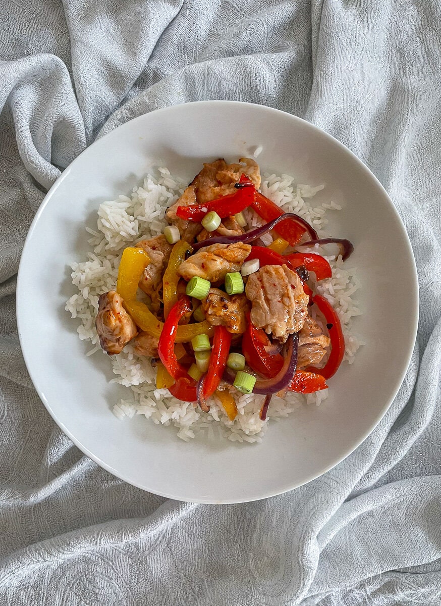 chicken and peppers in honey chilli sauce served with rice in white bowl.