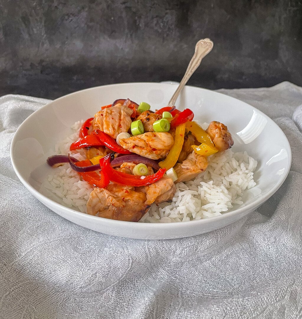 chicken and peppers in honey chilli sauce served with rice in white bowl.