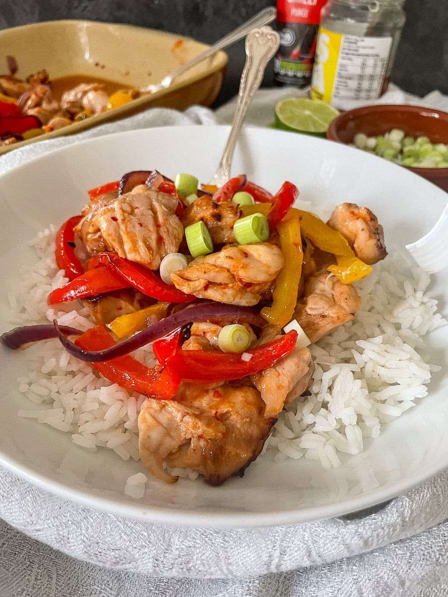 chicken and peppers in honey chilli sauce served with rice in white bowl. Close up.