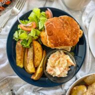 katsu curry burger on plate with salad, wedges and coleslaw.
