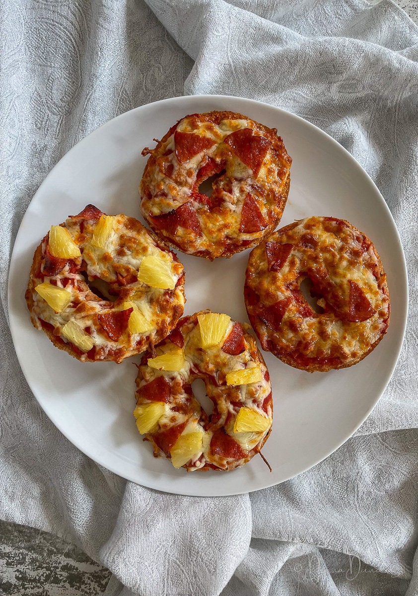 pizza bagels with pepperoni and pineapple on plate.