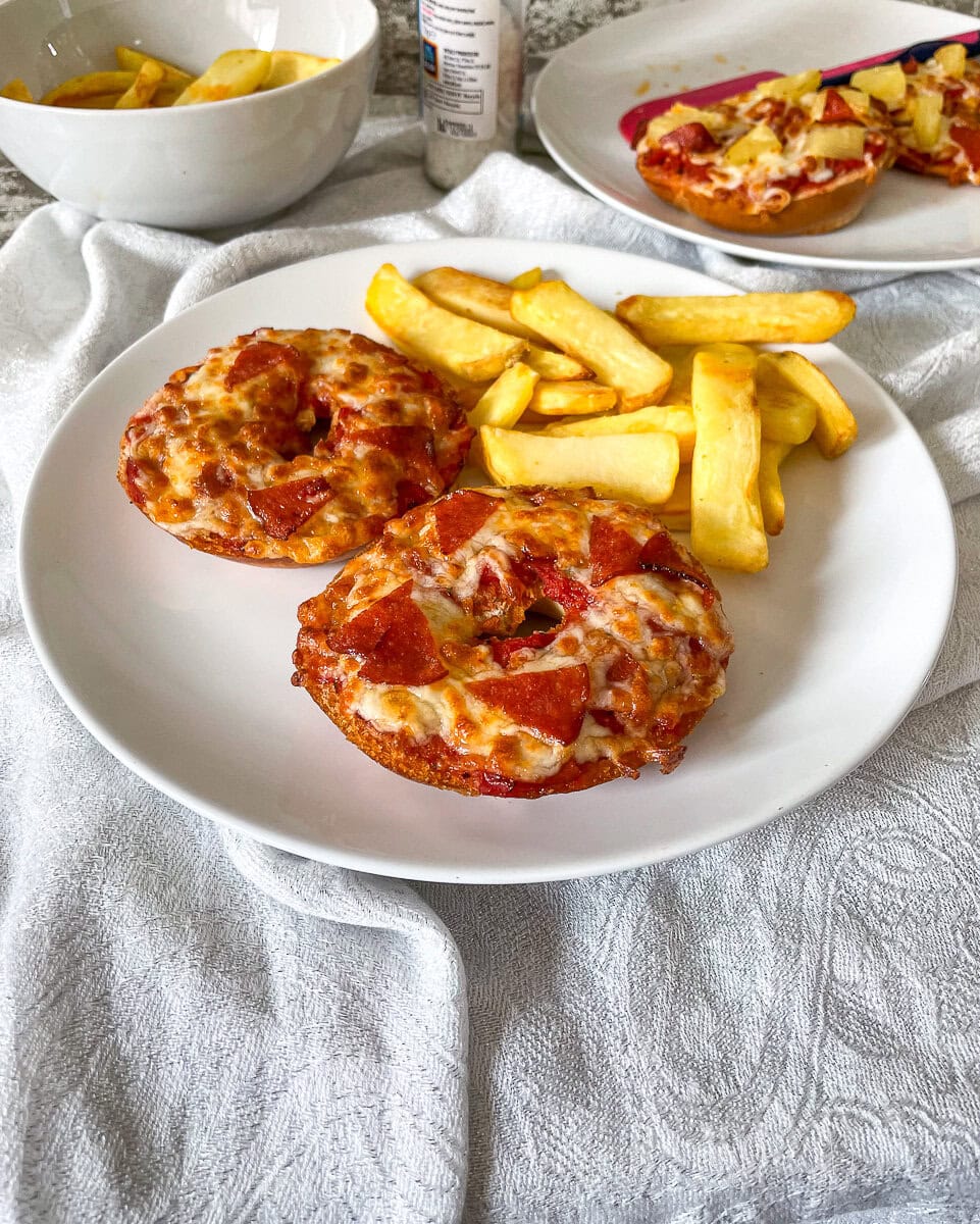 two halves of a pizza bagel on a plate with chips.