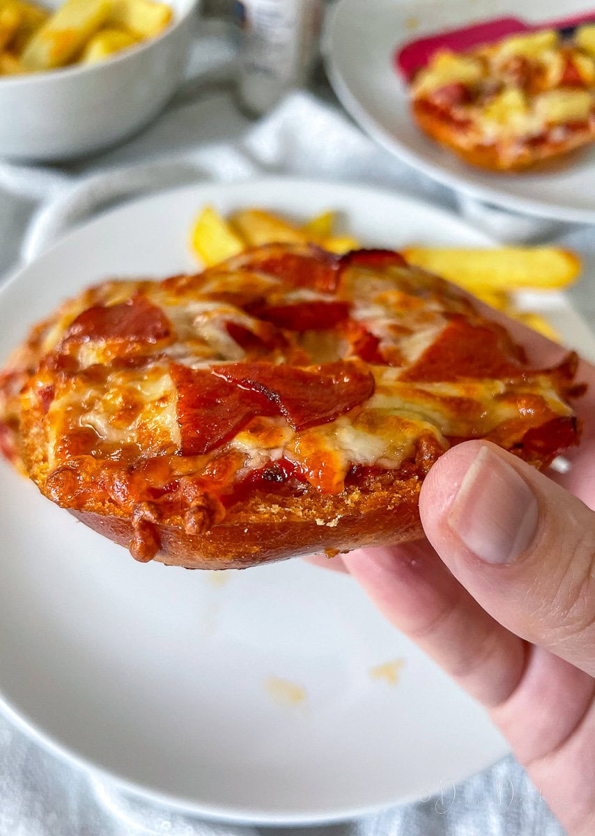 hand holding pizza bagel, side view. Plate in the background.
