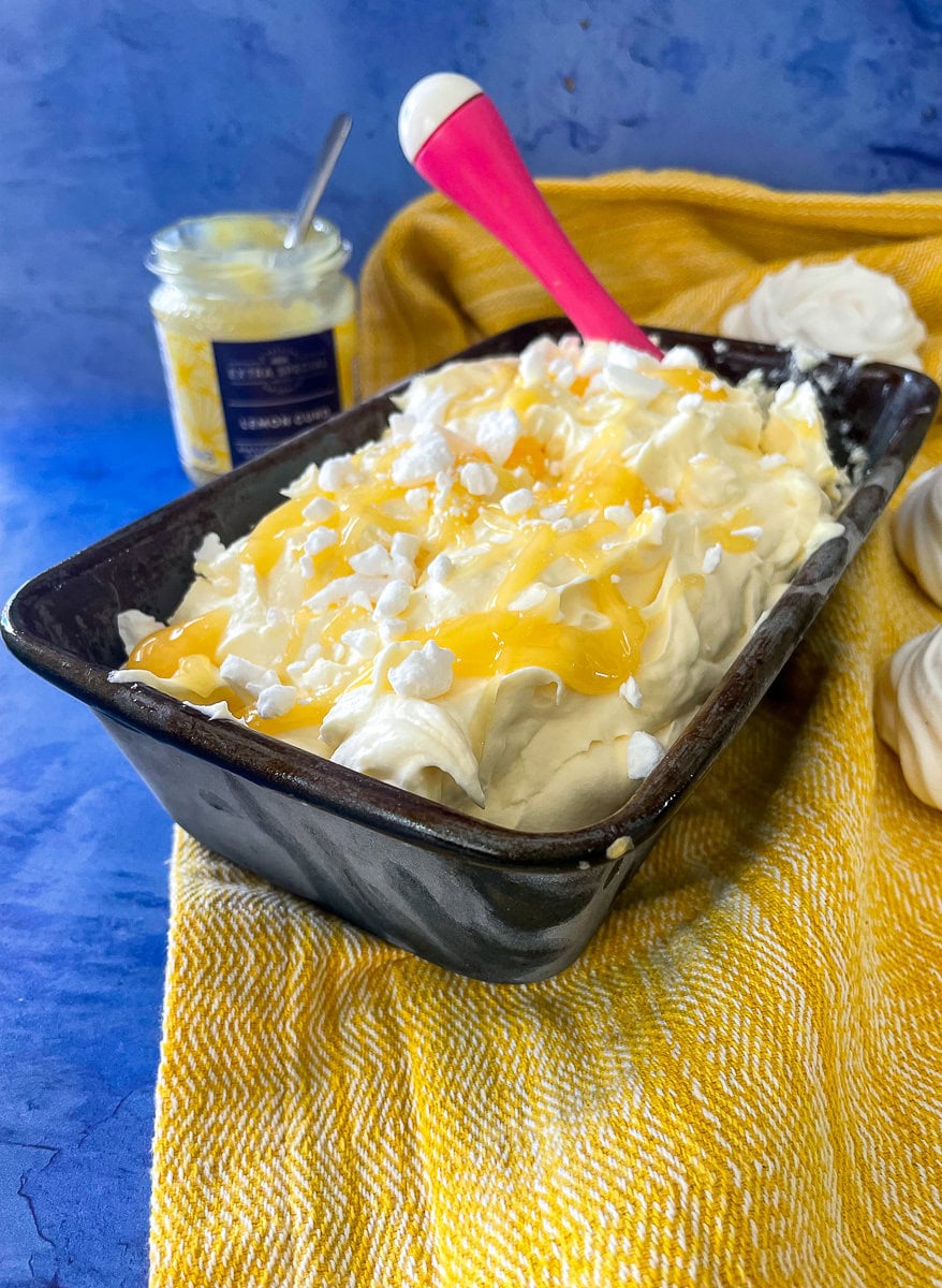 no-churn lemon meringue ice cream in loaf tin. Lemon curd and meringue nests also on table.