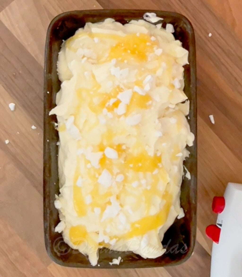 unfrozed ice cream topped with lemon curd and pieces of meringue in loaf pan.