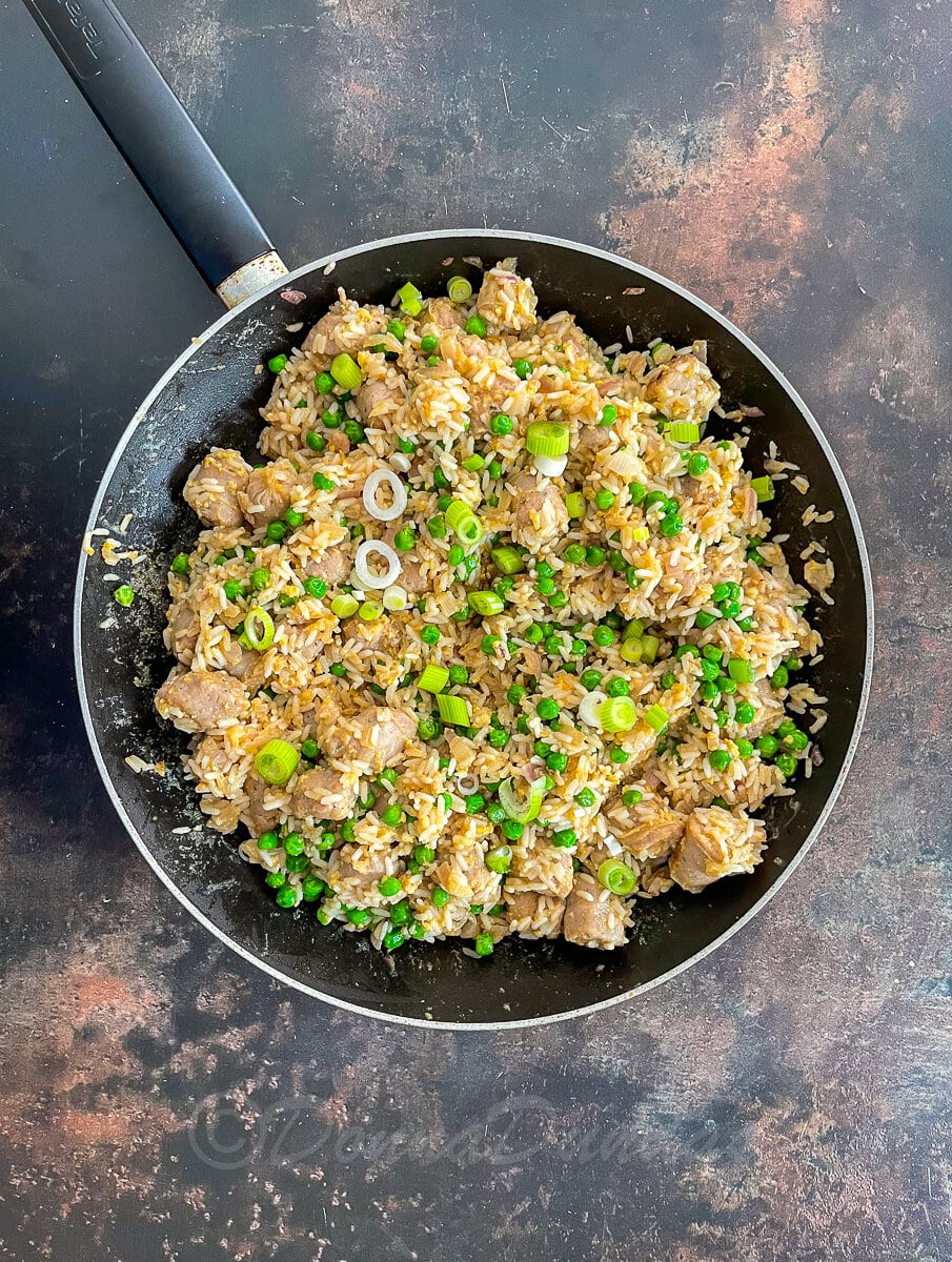 cooked fried rice with sausages, peas and spring onions in large frying pan.