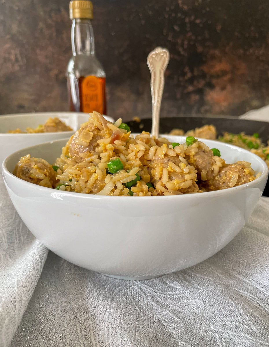 fried rice, sausage and peas in small white bowl with fork.