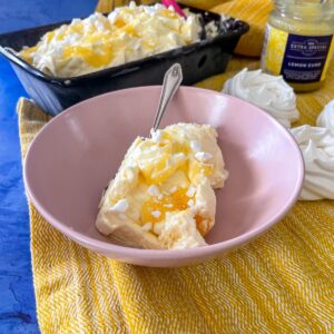 Ice cream in bowl topped with lemon curd and meringue. Rest of ice cream in loaf tin in the background. Lemon curd and merignue nests also on table.