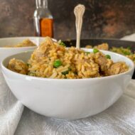 fried rice, sausage and peas in small white bowl with fork.